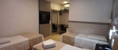 A hotel room with two single beds, a small desk, a chair, and a TV.