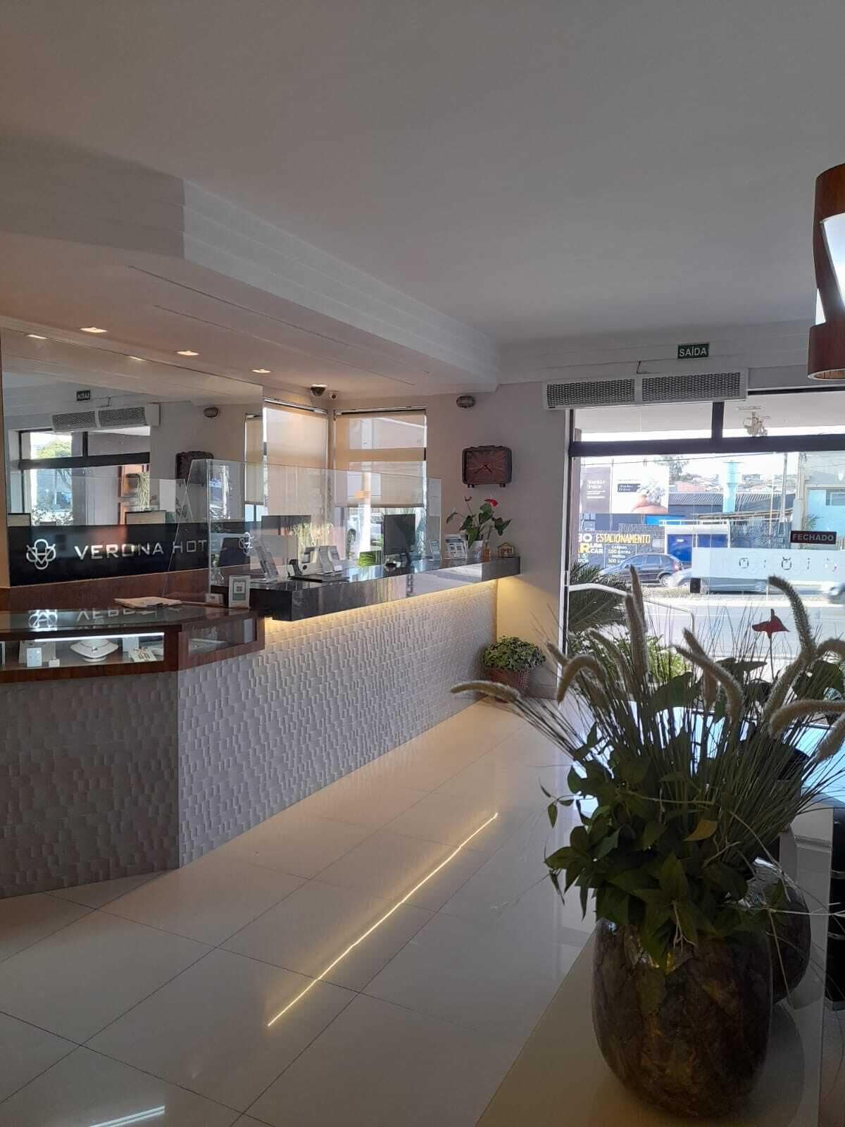 Zona de recepción de hotel con diseño moderno, que incluye un mostrador de recepción, un reloj y vistas a la calle.