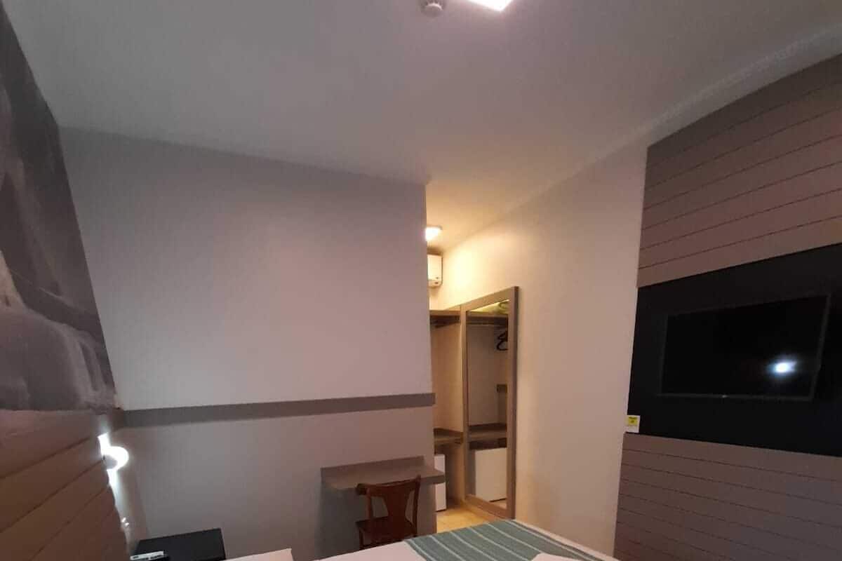 Hotellihuone, jossa on suuri sänky, seinälle asennettu televisio ja pieni pöytä tuolilla.