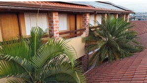 Un bâtiment avec un toit recouvert de tuiles rouges, des murs en briques et un balcon orné de plantes tropicales.