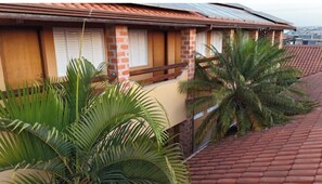 Un bâtiment avec un toit recouvert de tuiles rouges, des murs en briques et un balcon orné de plantes tropicales.