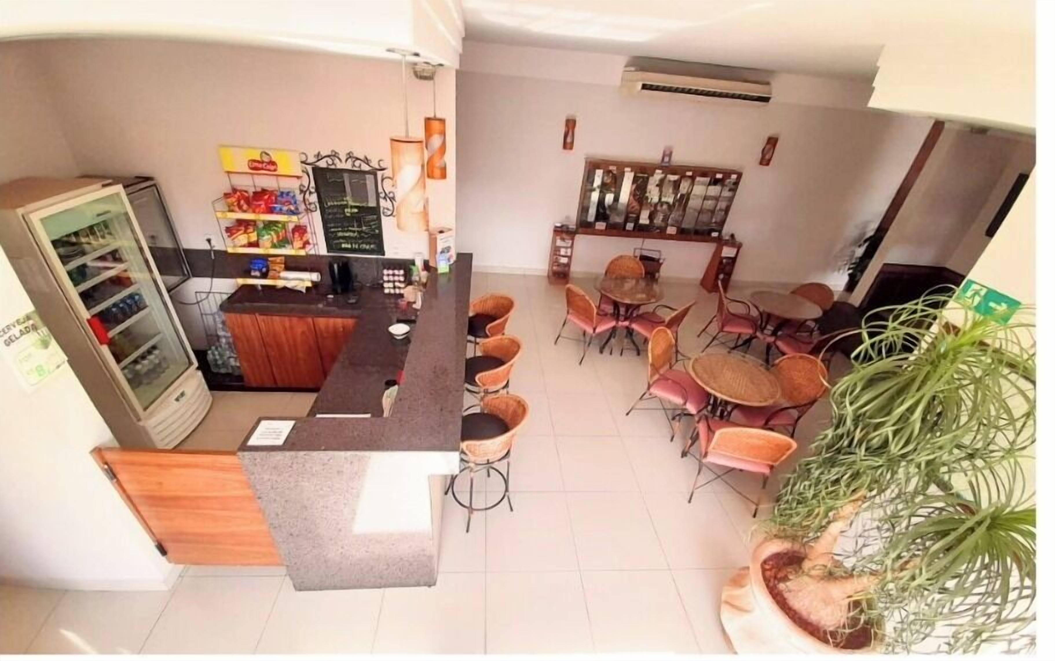 Cafetería con mostrador, sillas, refrigerador y una planta.