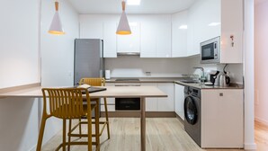 A compact kitchen with a washing machine, microwave, and a small refrigerator. There are two chairs and a table.