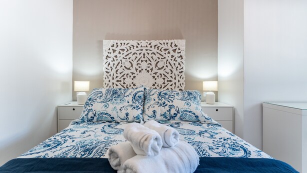 A neatly made bed with a patterned bedspread and pillows, a decorative headboard, and bedside lamps.