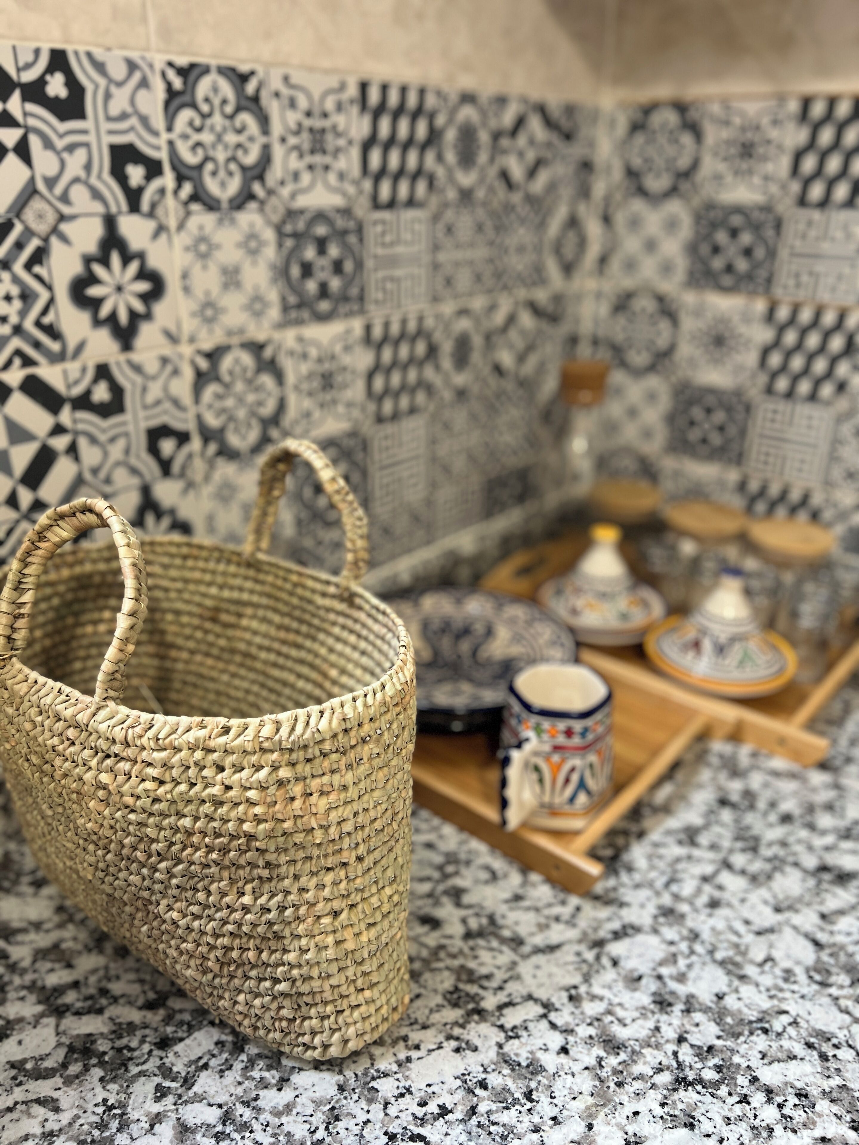 Una cesta tejida sobre una encimera de granito con un salpicadero de azulejos con diseños geométricos.