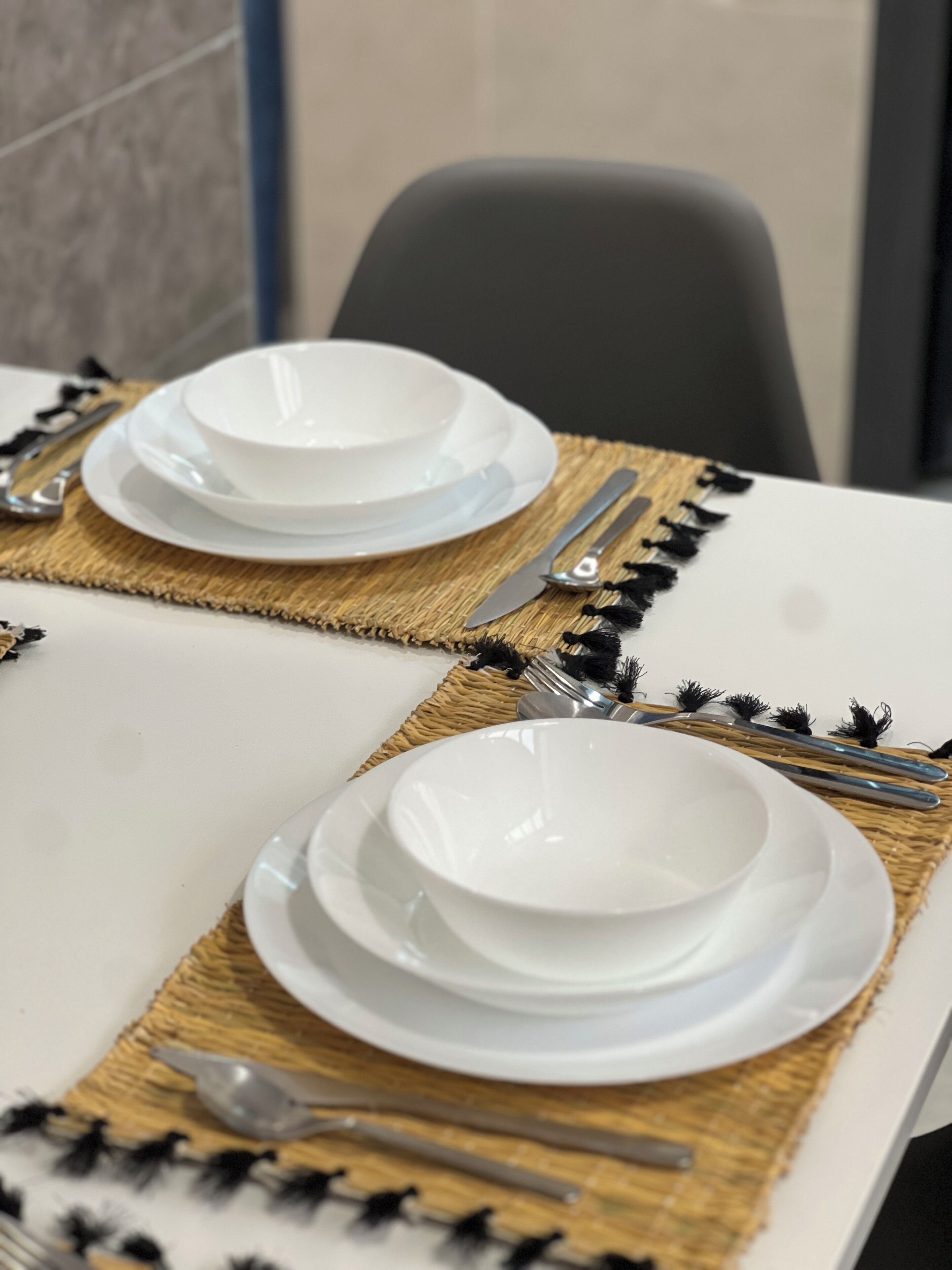 A table set with white plates, silverware, and a woven placemat.