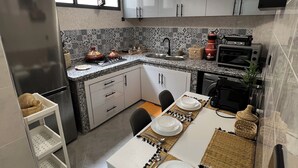 A modern kitchen with white cabinets, a built-in oven, a microwave, and a dining area set for four.