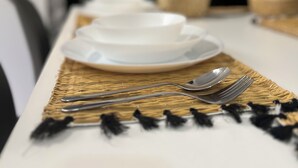 A dining table set with white plates, silverware, and a woven placemat.