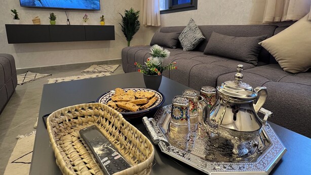A modern living room with a flat-screen TV, a sofa, a coffee table with decorative items, and a window with curtains.