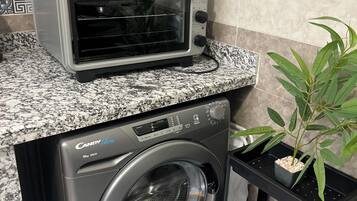 Une cuisine compacte équipée d’un four grille-pain, d’un lave-linge et d’une plante en pot.