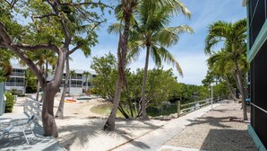 A pathway lined with palm trees and a small pond, leading to a building with a white fence and a dock. - Tropical 2BR/2BA Getaway in Gorgeous Key Largo, Pool, Kayak, Lagoon, Marina, (Key Largo)
