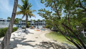 A beach with lounge chairs, a small pool, and a building with balconies in the background. - Tropical 2BR/2BA Getaway in Gorgeous Key Largo, Pool, Kayak, Lagoon, Marina, (Key Largo)