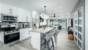 A modern kitchen with white cabinetry, stainless steel appliances, and a central island with bar stools. - Tropical 2BR/2BA Getaway in Gorgeous Key Largo, Pool, Kayak, Lagoon, Marina, (Key Largo)