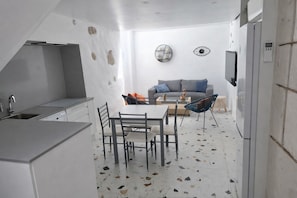A compact kitchen with a dining area, a gray sofa, and a wall-mounted TV.