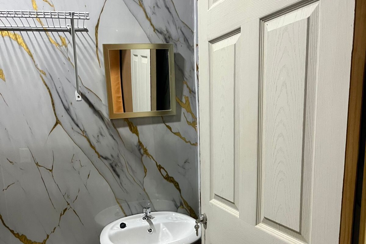 Een badkamer met een marmeren wand, een wastafel op voetstuk, een toilet en een deur.