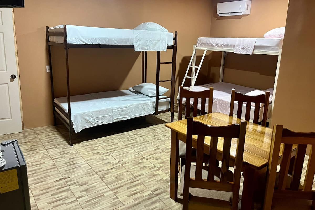 Une chambre avec un lit superposé, une table et des chaises en bois, une échelle et un appareil de climatisation.