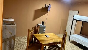 A compact room with a wooden table, a bunk bed, a small kitchenette, and a TV mounted on the wall. - Luisito steak house & hotel (La Fortuna)