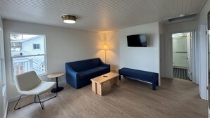 A modern living room with a blue sofa, a wooden coffee table, a white armchair, and a TV mounted on the wall.