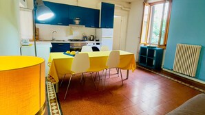 A compact kitchen with blue cabinets, a dining table with yellow chairs, and a large lamp. - Apartment with balcony in historic building, 100m from the Arena (Verona)