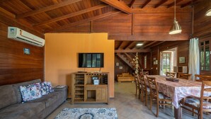 Una sala de estar acogedora con un sofá, televisión, mueble de madera para entretenimiento y una mesa de comedor con sillas.