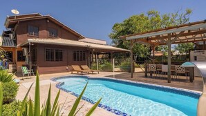 Una casa con piscina, mobiliario exterior y una pérgola.