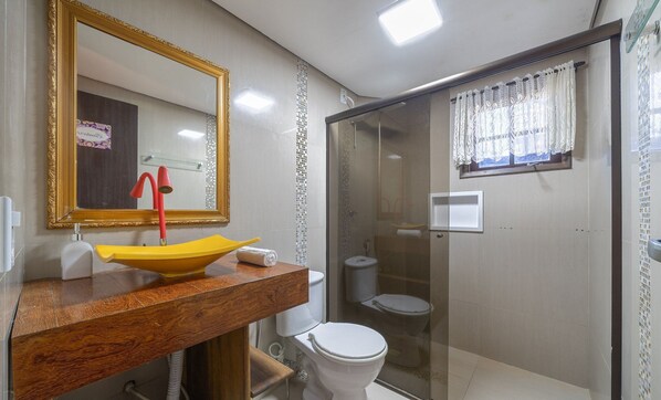 Une salle de bain avec un lavabo jaune, des toilettes blanches et une douche fermée par une paroi de verre.