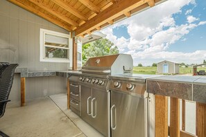 A covered outdoor kitchen area with a stainless steel stove and oven, a window, and a view of the surrounding landscape. - Koko House: Mountain Views, BBQ & Patio (Loma)