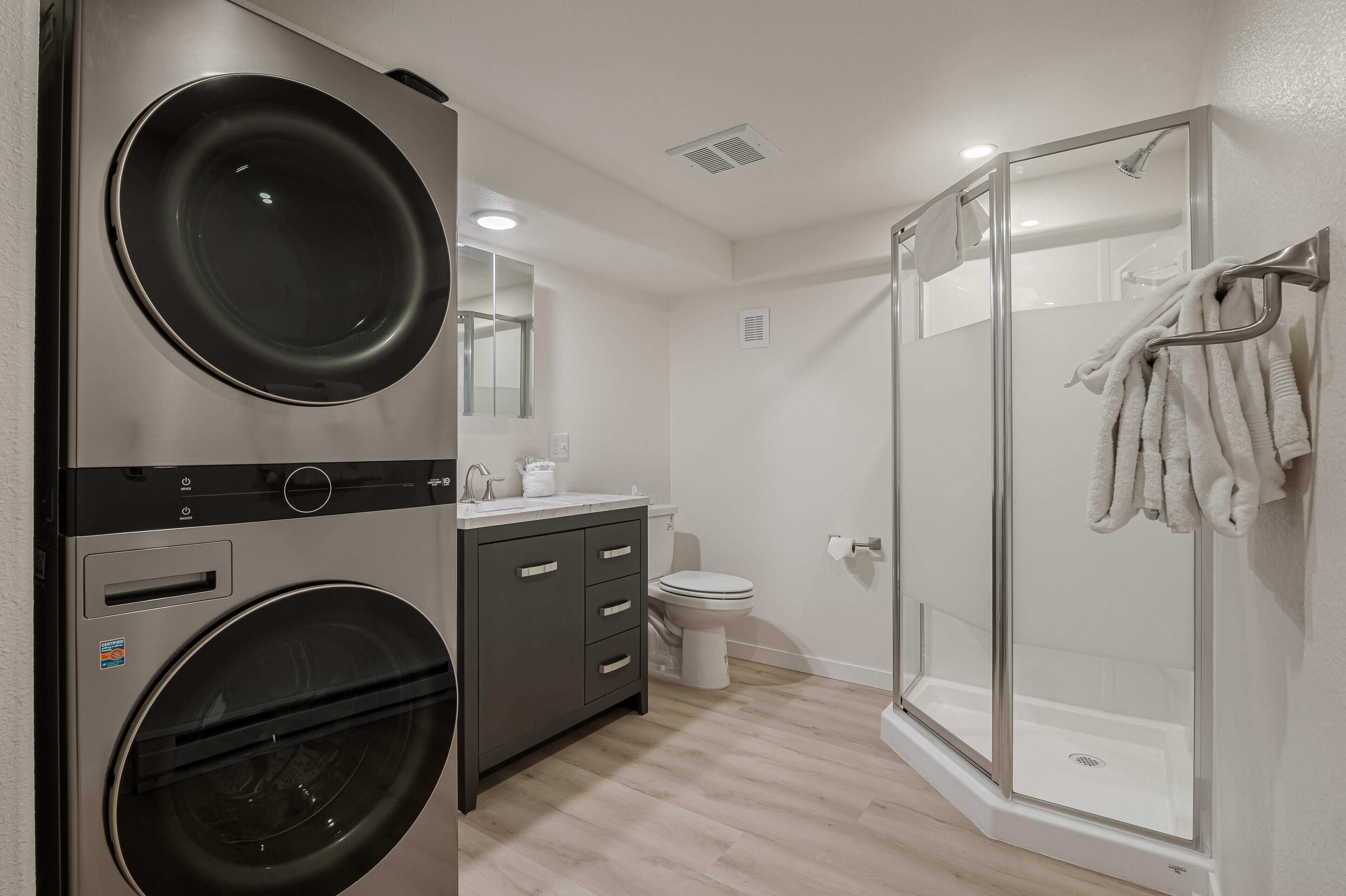 A modern bathroom with a built-in washer and dryer, a glass shower enclosure, and a toilet.