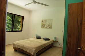 Un dormitorio con una cama, un ventilador de techo, una ventana y un cuadro en la pared.