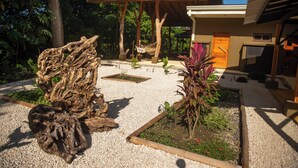 A modern building with a covered patio area, surrounded by a garden with various plants and a large piece of driftwood. - Charming country house in  Playa Órganos Paquera in the middle of nature (Paquera)