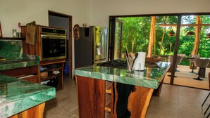 A kitchen with a large island, stainless steel appliances, and a view of a lush garden. - Charming country house in  Playa Órganos Paquera in the middle of nature (Paquera)