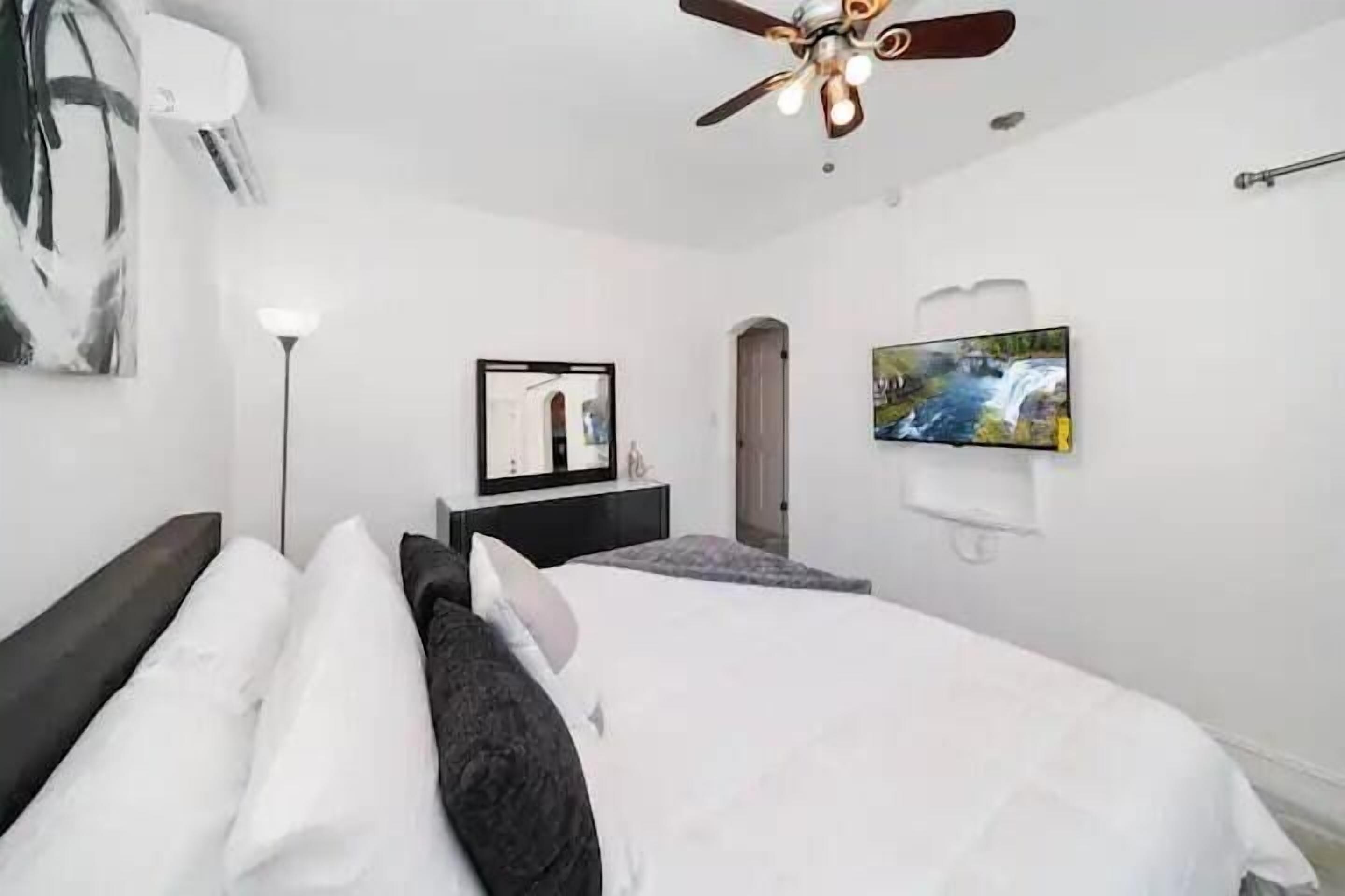Quarto de hotel moderno com uma cama grande, ventoinha no teto, televisão presa na parede e um quadro na parede.
