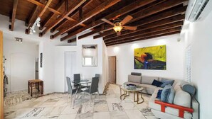 A spacious living room with a high ceiling, a dining area with a glass table and chairs, a sofa with cushions, and a large abstract painting on the wall. - Waterways Komffy (Hollywood)