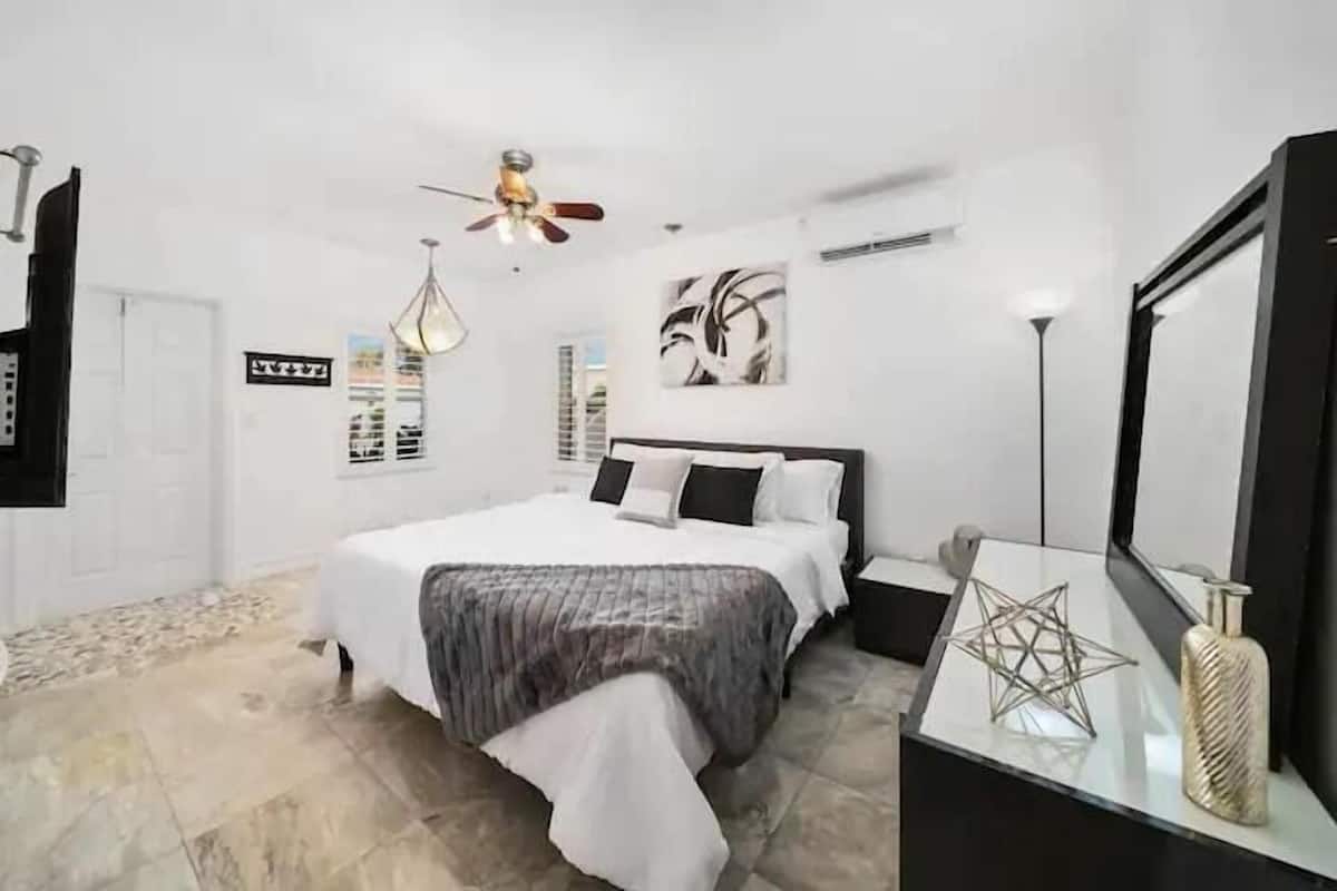 Un dormitorio con una cama, ventilador de techo, aire acondicionado de pared y un objeto decorativo con forma de estrella sobre una mesita de noche.