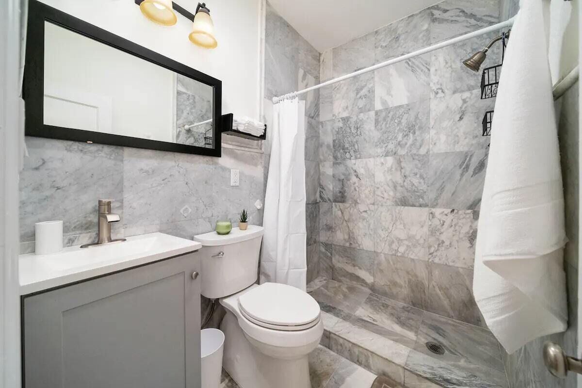 Un baño con ducha de mármol, inodoro y lavamanos con espejo.