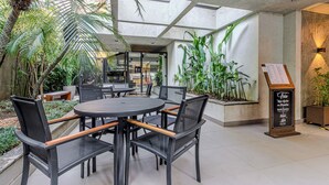 An outdoor seating area with round tables and chairs, surrounded by potted plants and a menu board. - Charlie Poeta Drummond Jardins (São Paulo)