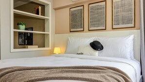 A hotel room with a bed, a shelf with books and a plant, and three framed artworks on the wall. - Charlie Poeta Drummond Jardins (São Paulo)