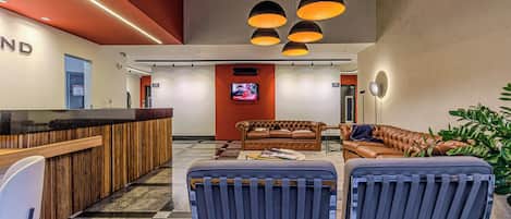 A modern lobby with a reception desk, seating area, and a television screen.