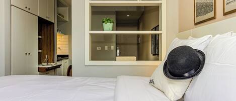 Habitación de hotel con cama, armario, kitchenette pequeño y estante con planta y libros.