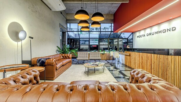 A modern lobby with leather sofas, a reception desk, and pendant lighting. - Charlie Poeta Drummond Jardins (São Paulo)