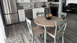 Une cuisine moderne avec des meubles blancs, des appareils en acier inoxydable et un coin repas comprenant une table ronde et des chaises.