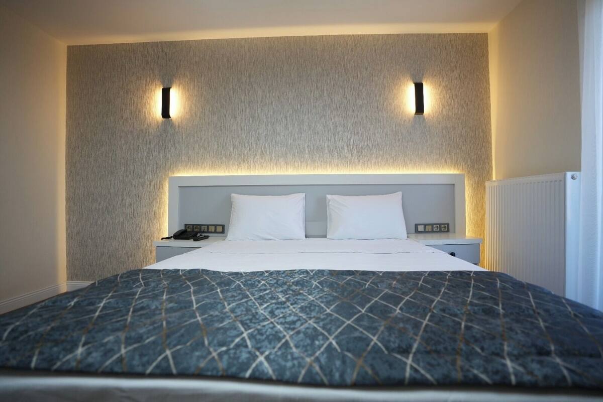 A modern hotel room with a large bed, two bedside tables, and a textured wall with integrated lighting.
