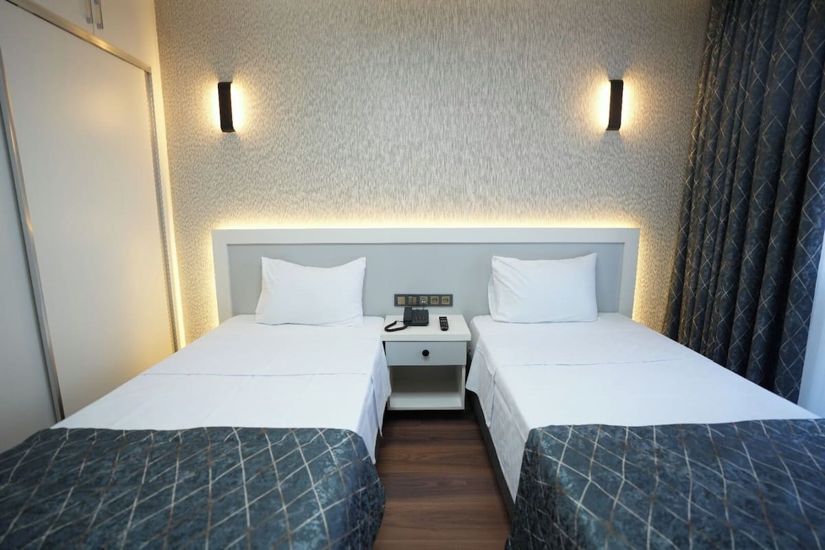 A hotel room with two beds, a nightstand with a phone, and wall-mounted lights.