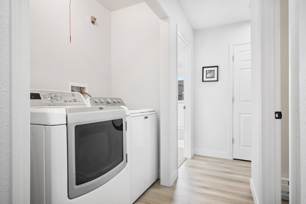A laundry room with a washer and dryer, a door leading to another room, and a light switch on the wall.