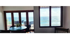 Una habitación con un ventanal grande con vista al océano, una mesa redonda con sillas y un pequeño florero con flores.