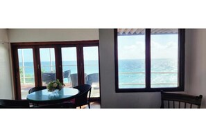 Una habitación con un ventanal grande con vista al océano, una mesa redonda con sillas y un pequeño florero con flores.