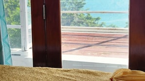 Una habitación con una cama, una puerta de madera y vista al océano.