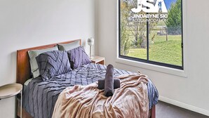 A bedroom with a bed, a nightstand, a lamp, and a window with a view of a grassy area and trees.