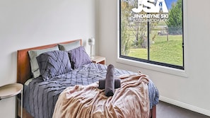 Une chambre à coucher comprenant un lit, une table de chevet, une lampe et une fenêtre donnant sur un espace verdoyant et des arbres.