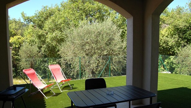 Un patio al aire libre con una mesa y sillas, rodeado de césped y un seto.